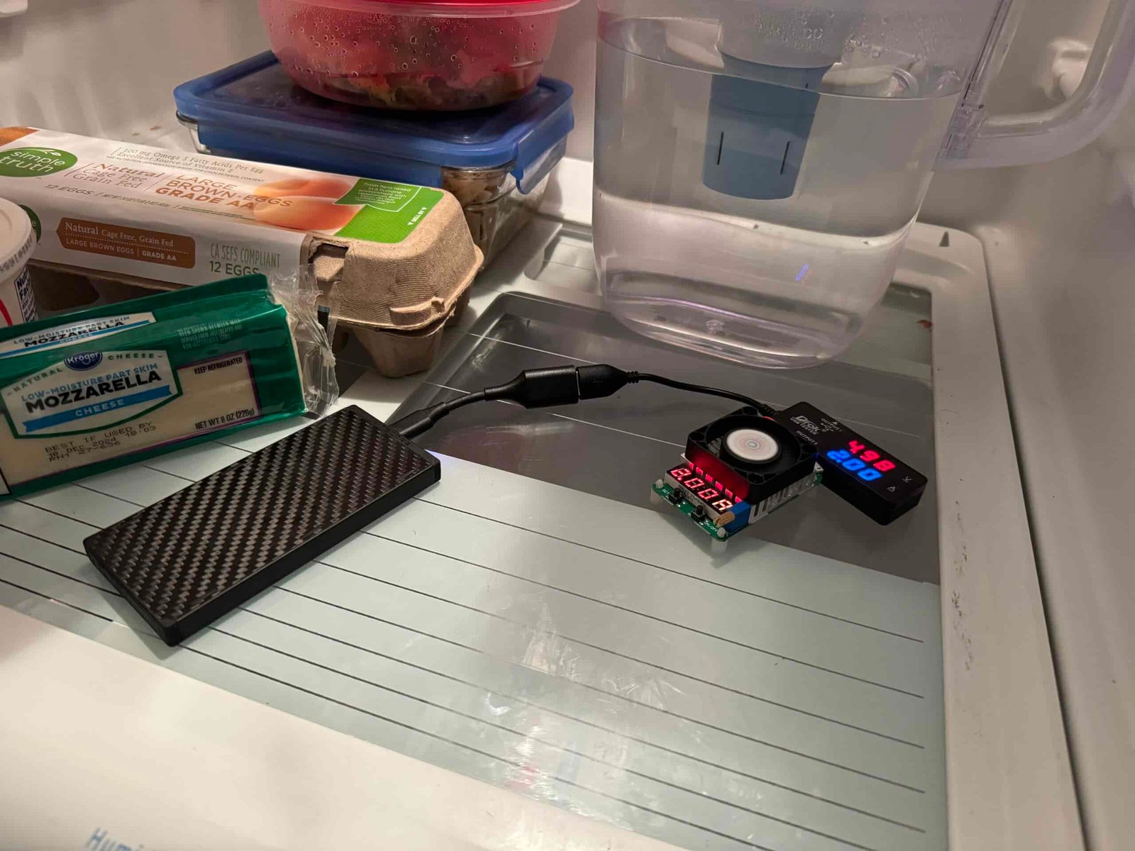 The Nitecore power bank is hooked up to a multimeter and dummy resistor load inside a refrigerator with food.