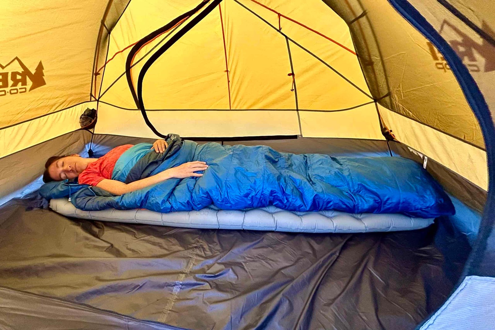 A person lies asleep in a tent, cozy in a sleeping bag on a thick air pad.