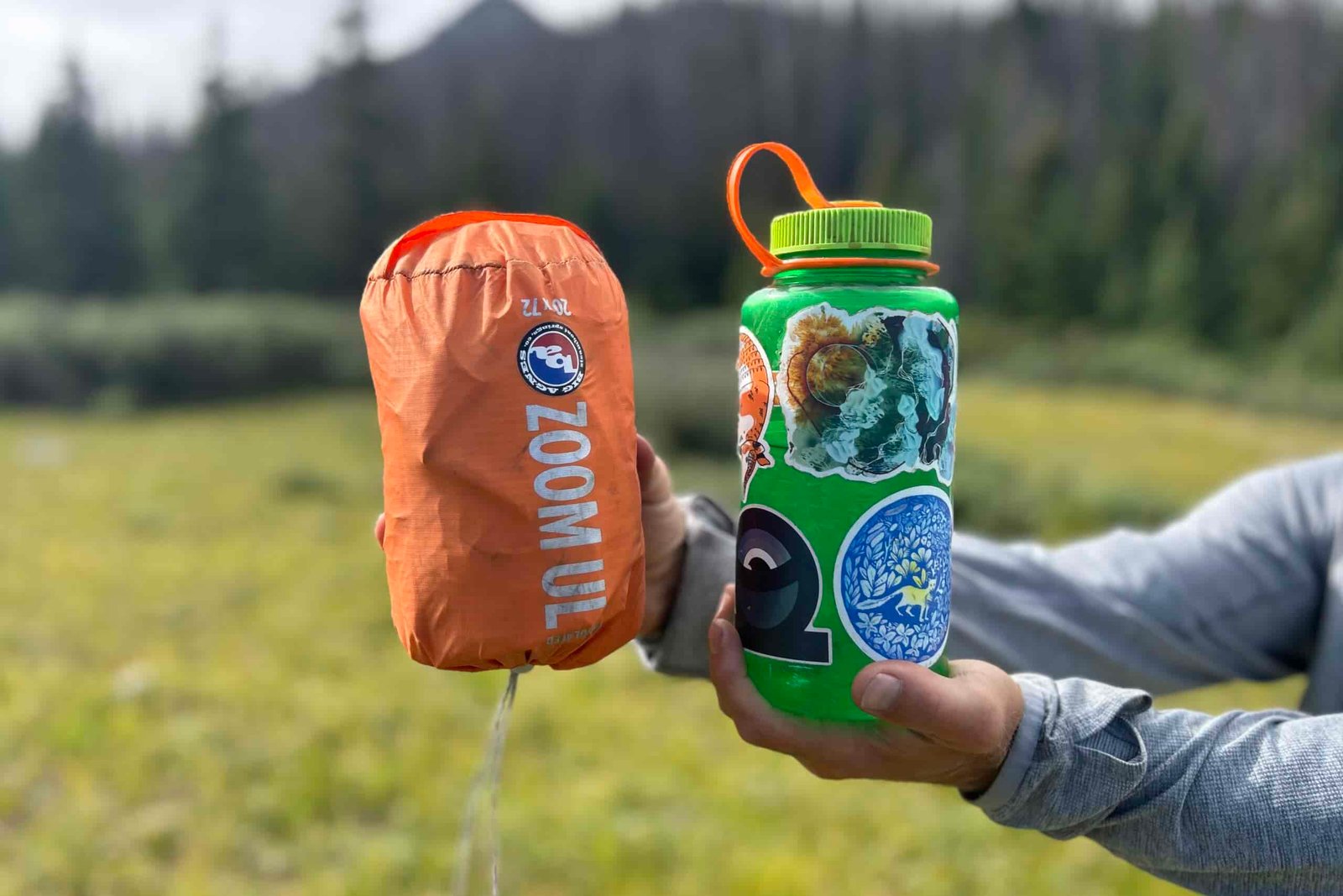 A person holds up an orange sleeping pad in it's compression sack next to a water bottle for a size comparison.