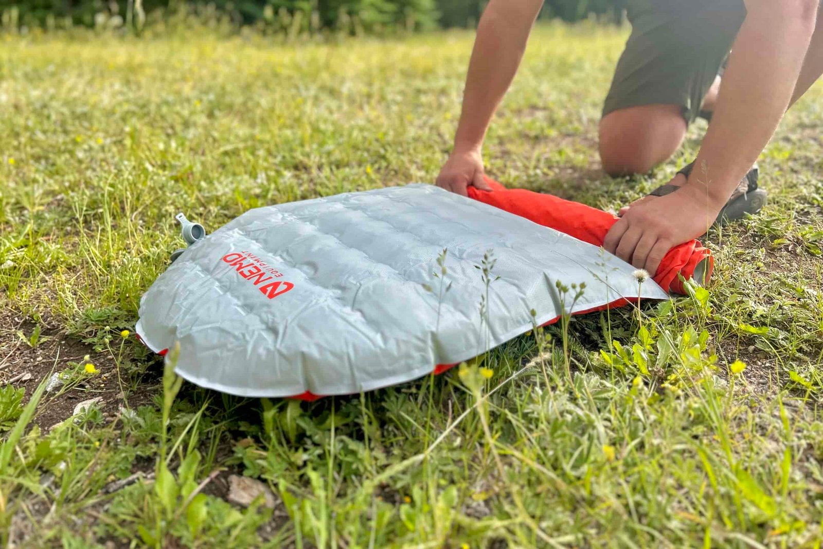A man rolls up an inflatable sleeping pad on the ground.