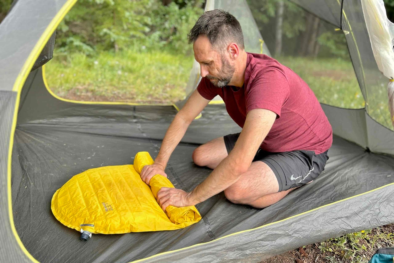 A man rolls up an inflatable sleeping pad in a tent.