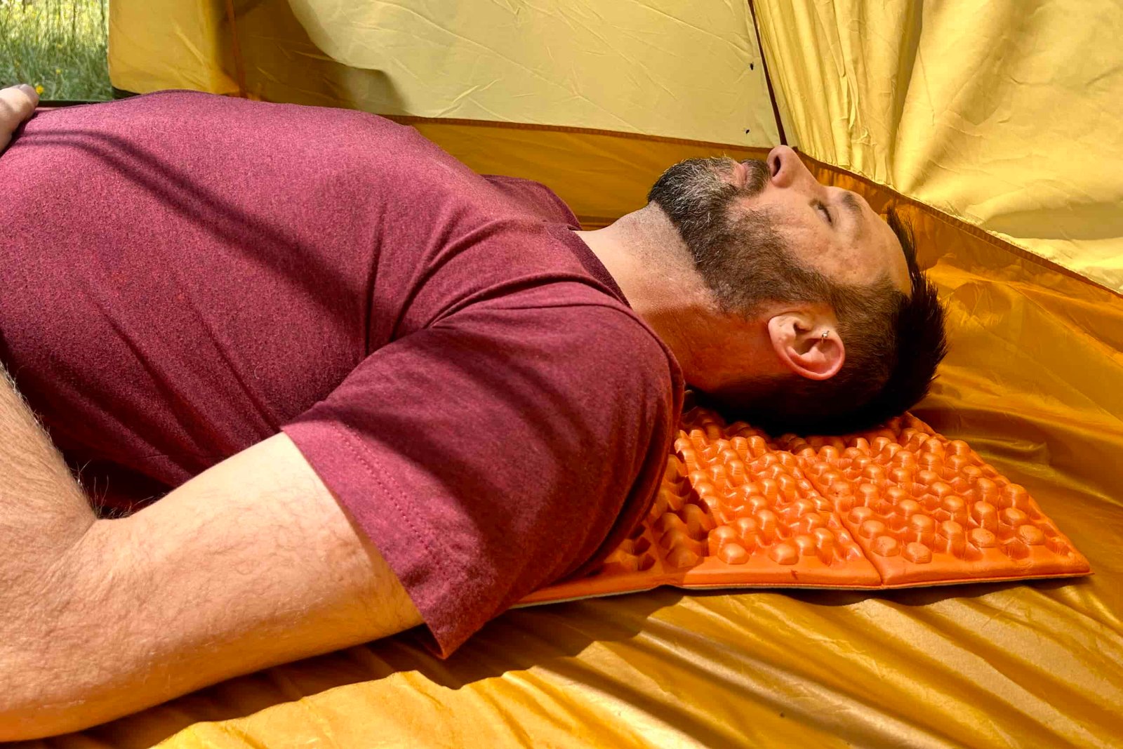 A man rests on a sleeping pad inside a tent.
