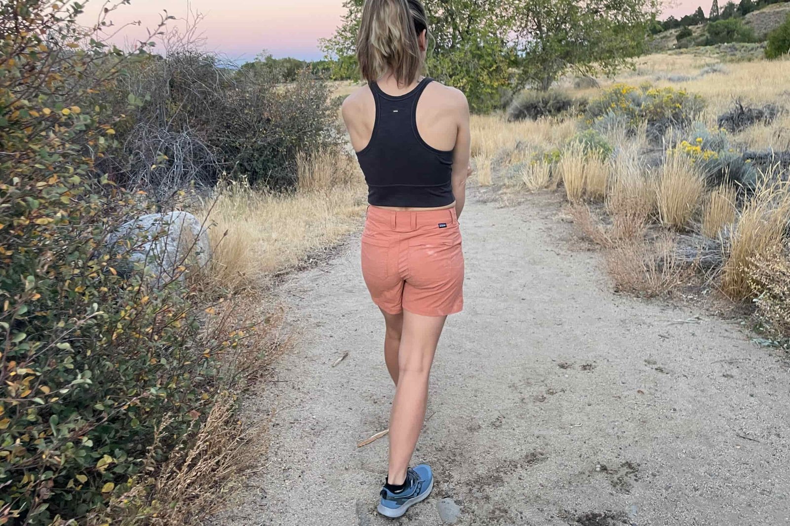 a person walking away from the camera on a sandy trail in sunset