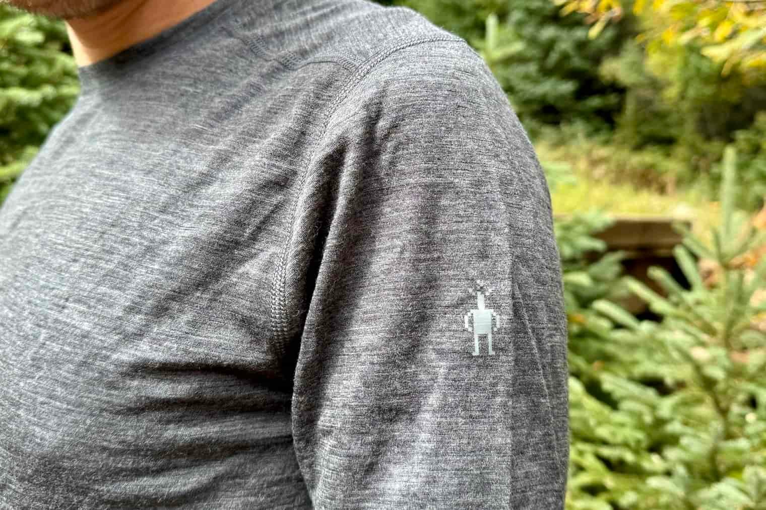 A close up of the shoulder logo on the Smartwool Classic All-Season base layer. Trees are in the background.