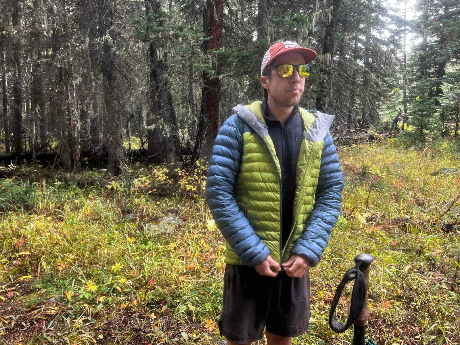 A hiker zips up a jacket over top of the Arc'teryx Rho Heavyweight Zip Neck base layer. Trees are in the background.
