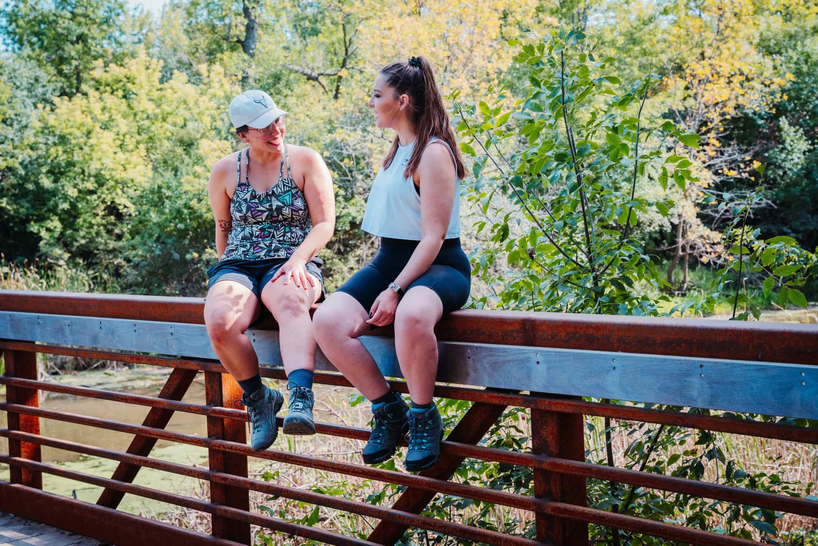 Two hikers sitting on a bridge wearing Keen Targhee IV WP and Merrell Moab 3 WP Women's Hiking Boots