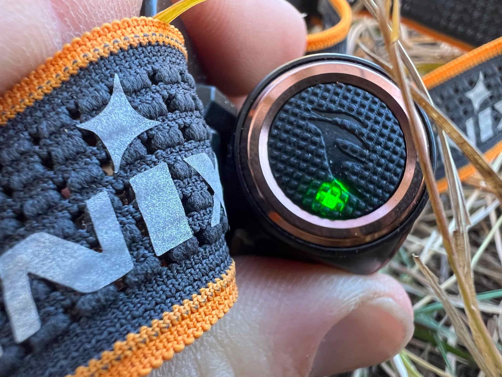 The image shows the power button of a Fenix HM50R V2.0 headlamp, with a green battery indicator light illuminated. The headlamp's strap, featuring the Fenix logo in white, is visible in the background.