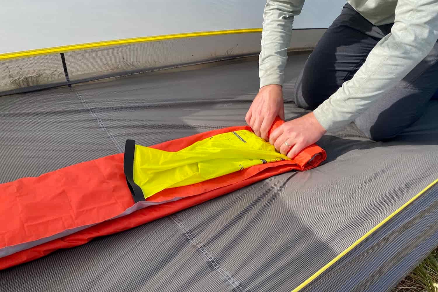 a backpacker rolls up their sleeping pad and vortex inflating sack inside an empty tent