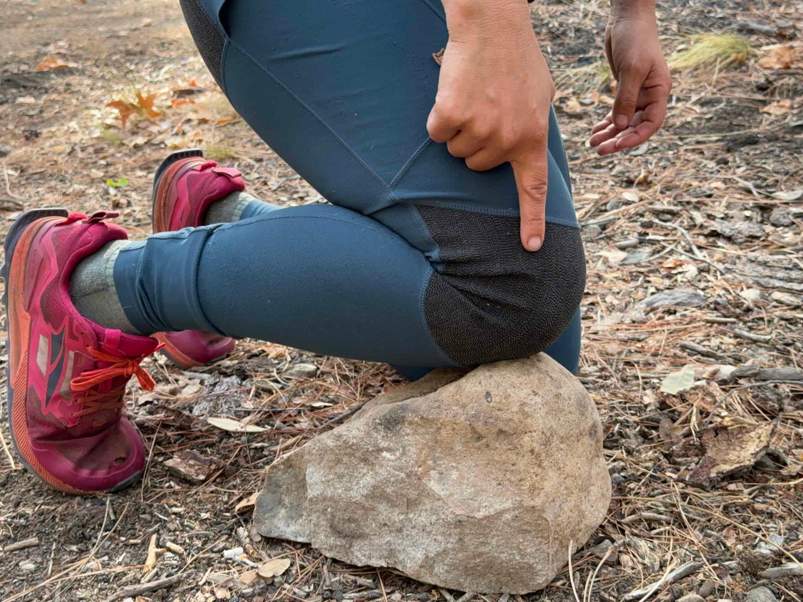 The reinforced knee of the Abisko leggings are resting on a rock with a finger pointing out this feature.