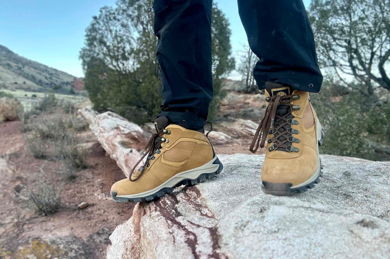 Close up from knees down of a person walking in hiking boots on a rock while the sun sets behind.
