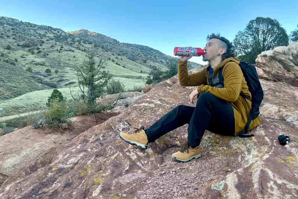 A man sits and drinks water at sunset in a desert setting.