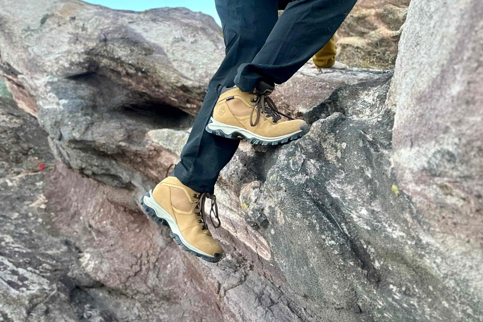 Close up from knees down of a person scrambling up a rock.