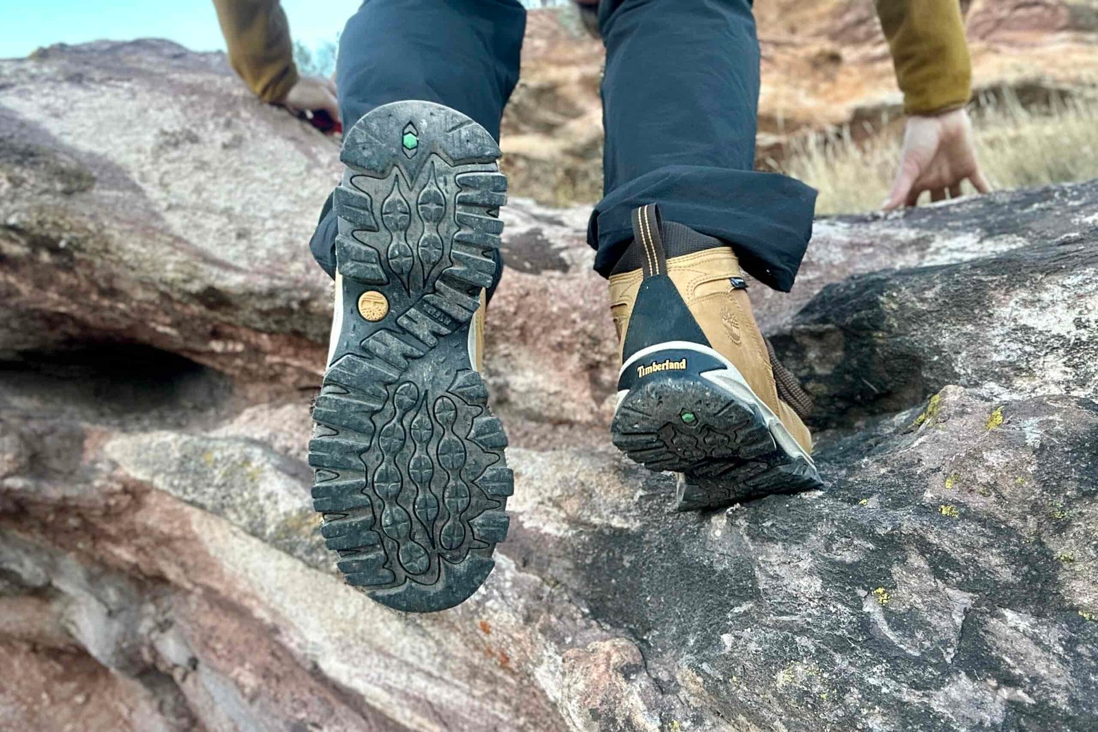 Close up from knees down of a person scrambling in hiking boots on a rock. You can see the traction well.