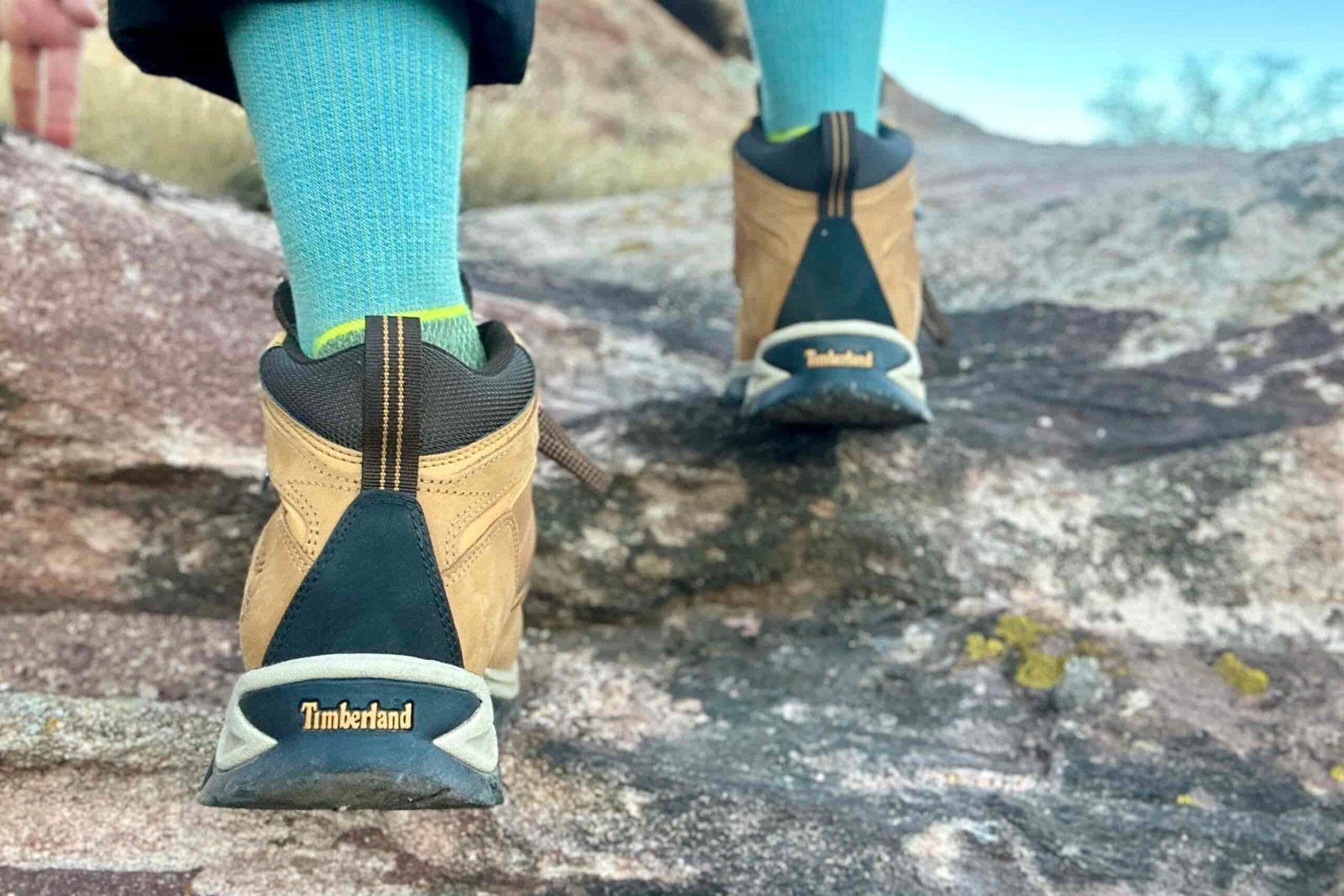 Close up from knees down of a person scrambling in hiking boots on a rock.