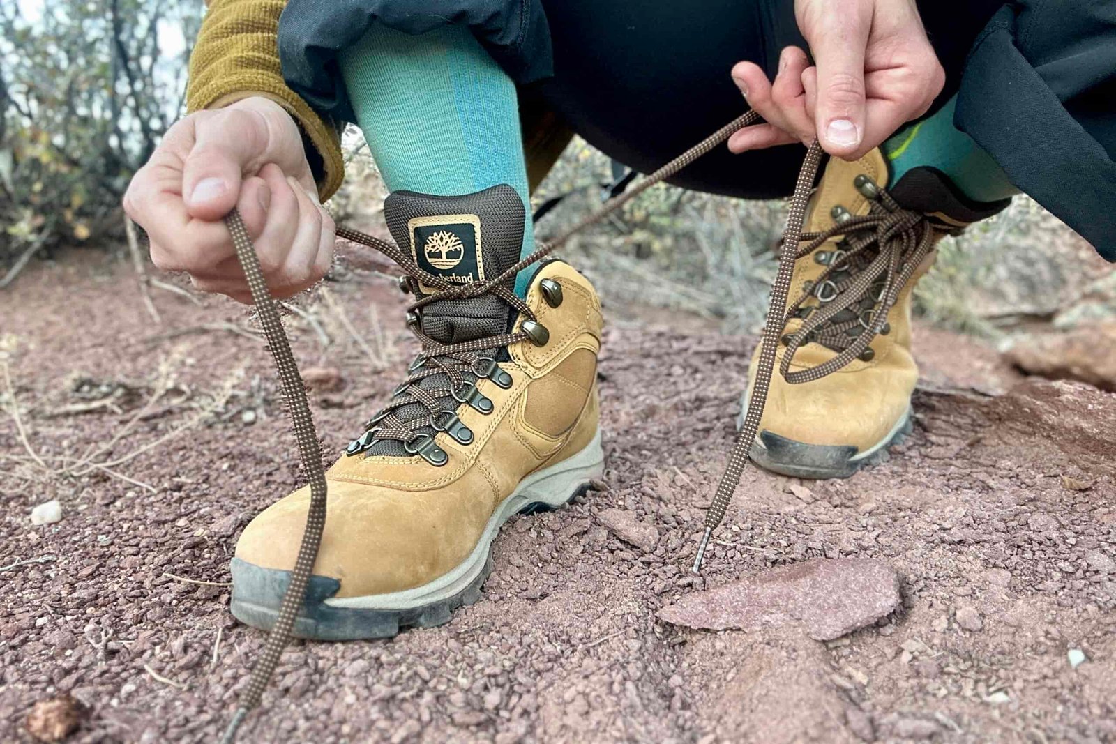 Close up from knees down of a person tying their hiking boots and the laces are very long.