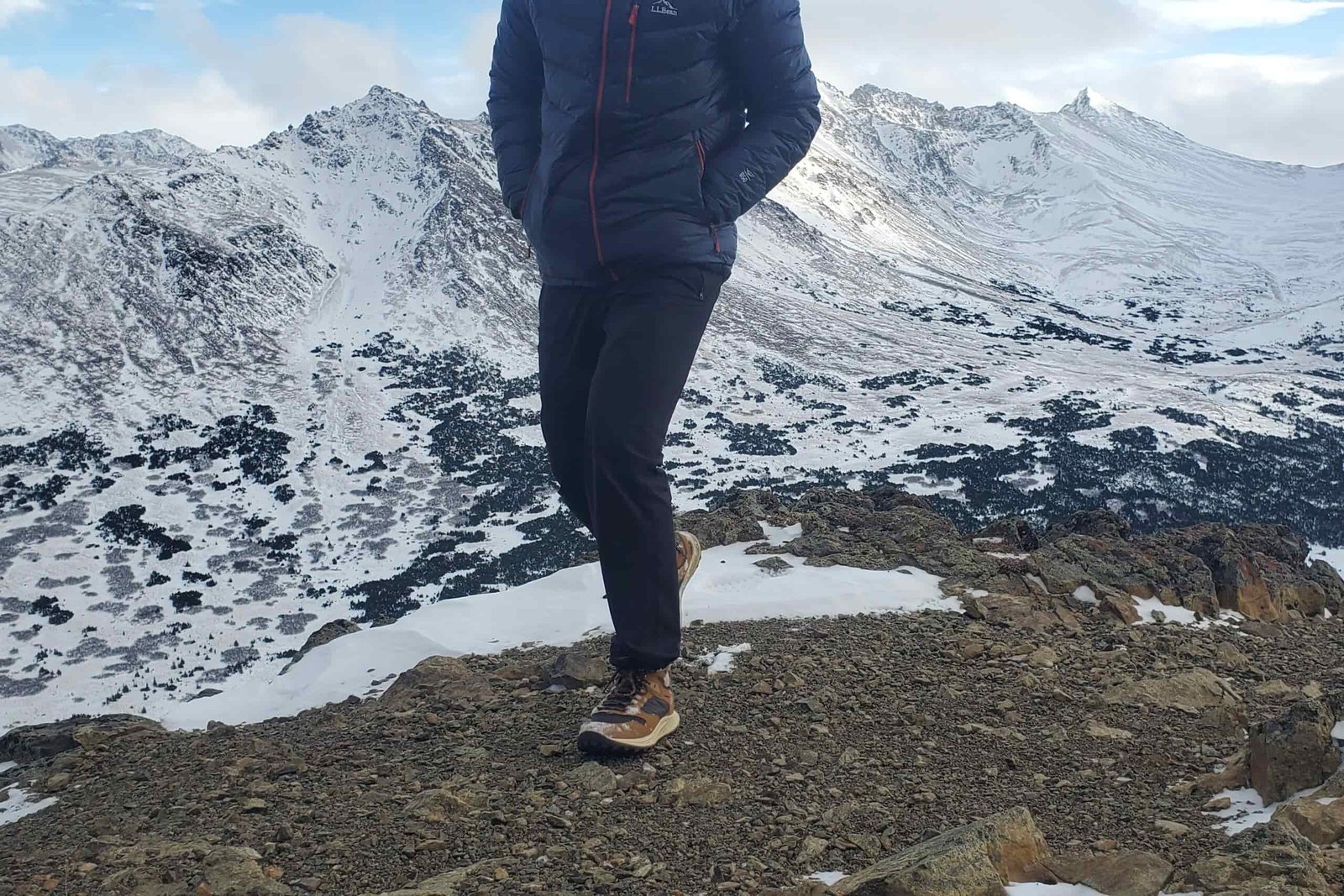 A man walks on rocks on a mountain peak.