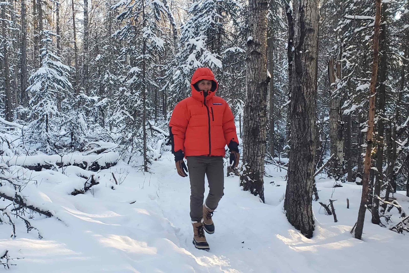A man walks in a red down jacket through a snowy forest