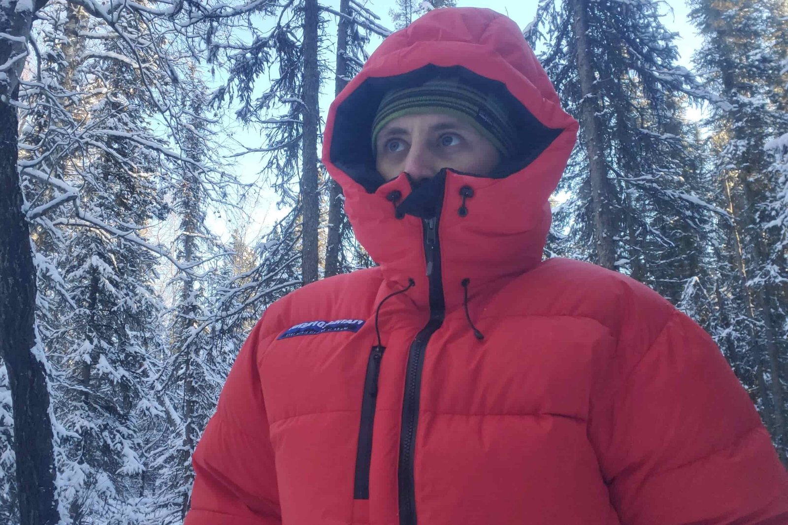 A man stands in a fully zipped and hooded down jacket.