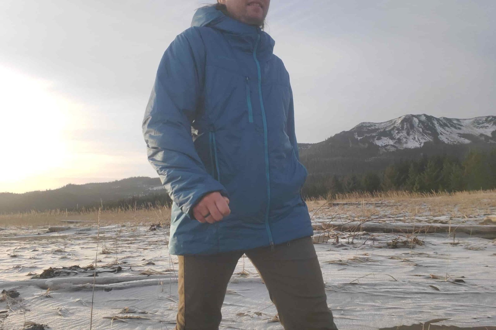 A closeup of the front of a puffy jacket in front of a mountain view.
