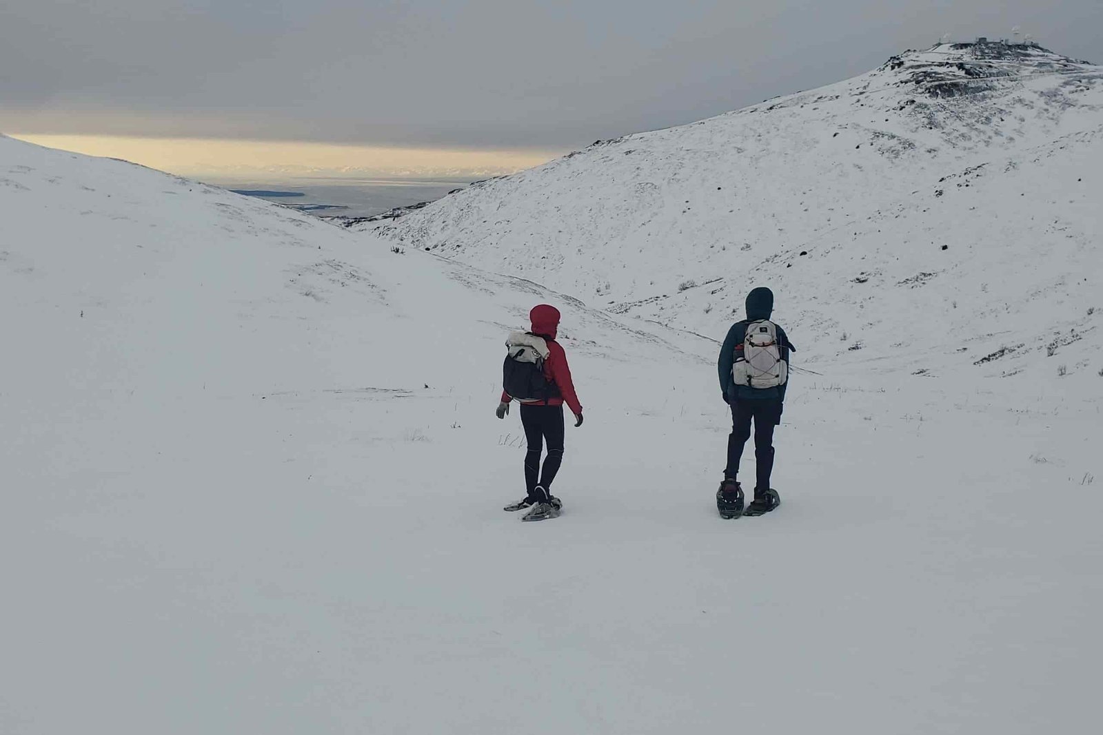 Two people walk down a mountainside in snowshoes.