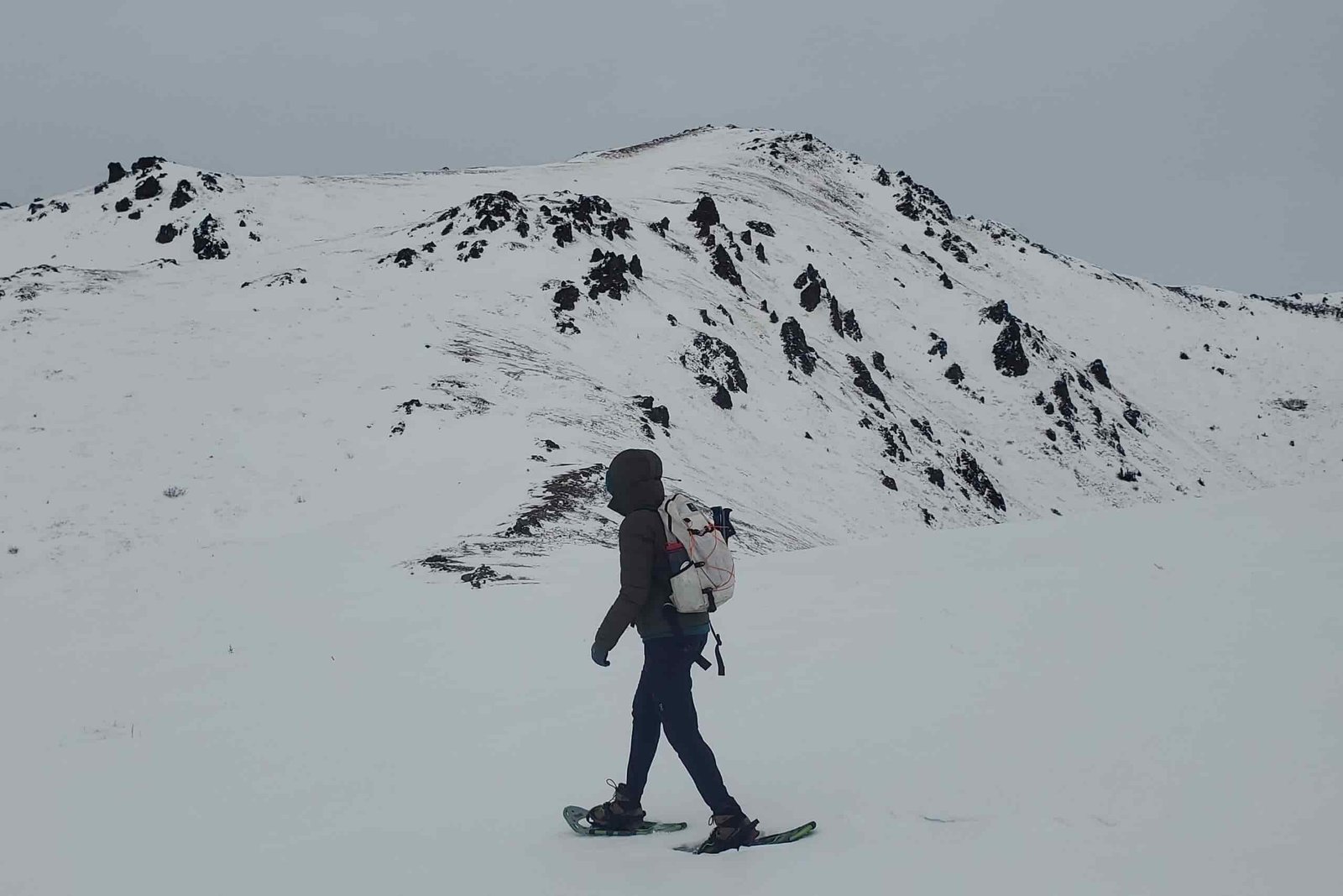 A woman walks past a mountain wearing snowshoes