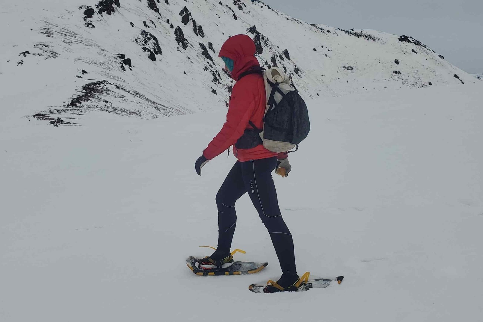 A woman walks through a mountain landscape wearing snowshoes.