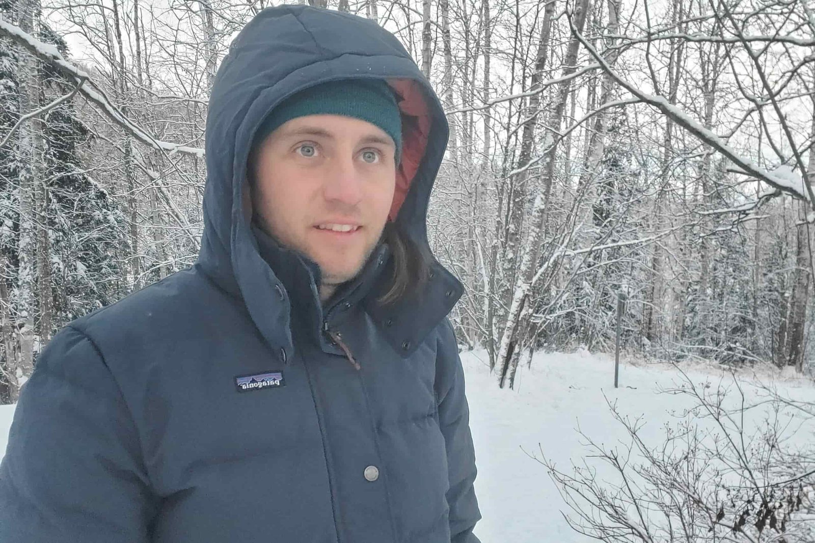 A man stands with his hood up in snowy woods
