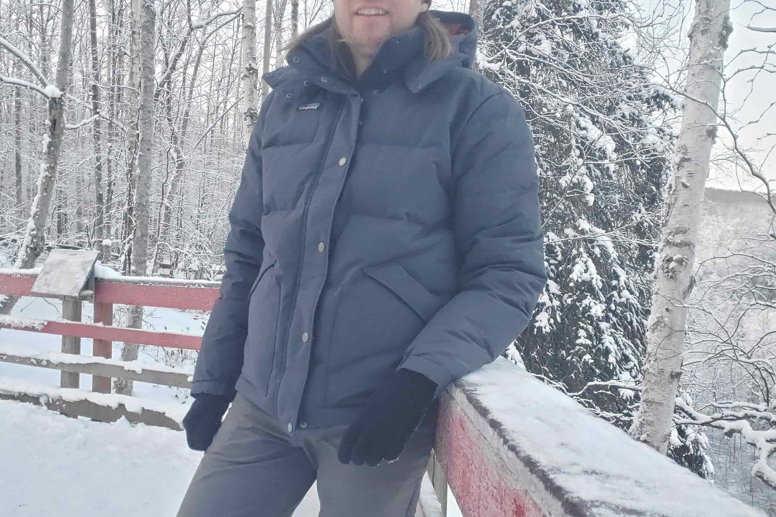 A man leans against a railing in a snowy forest.