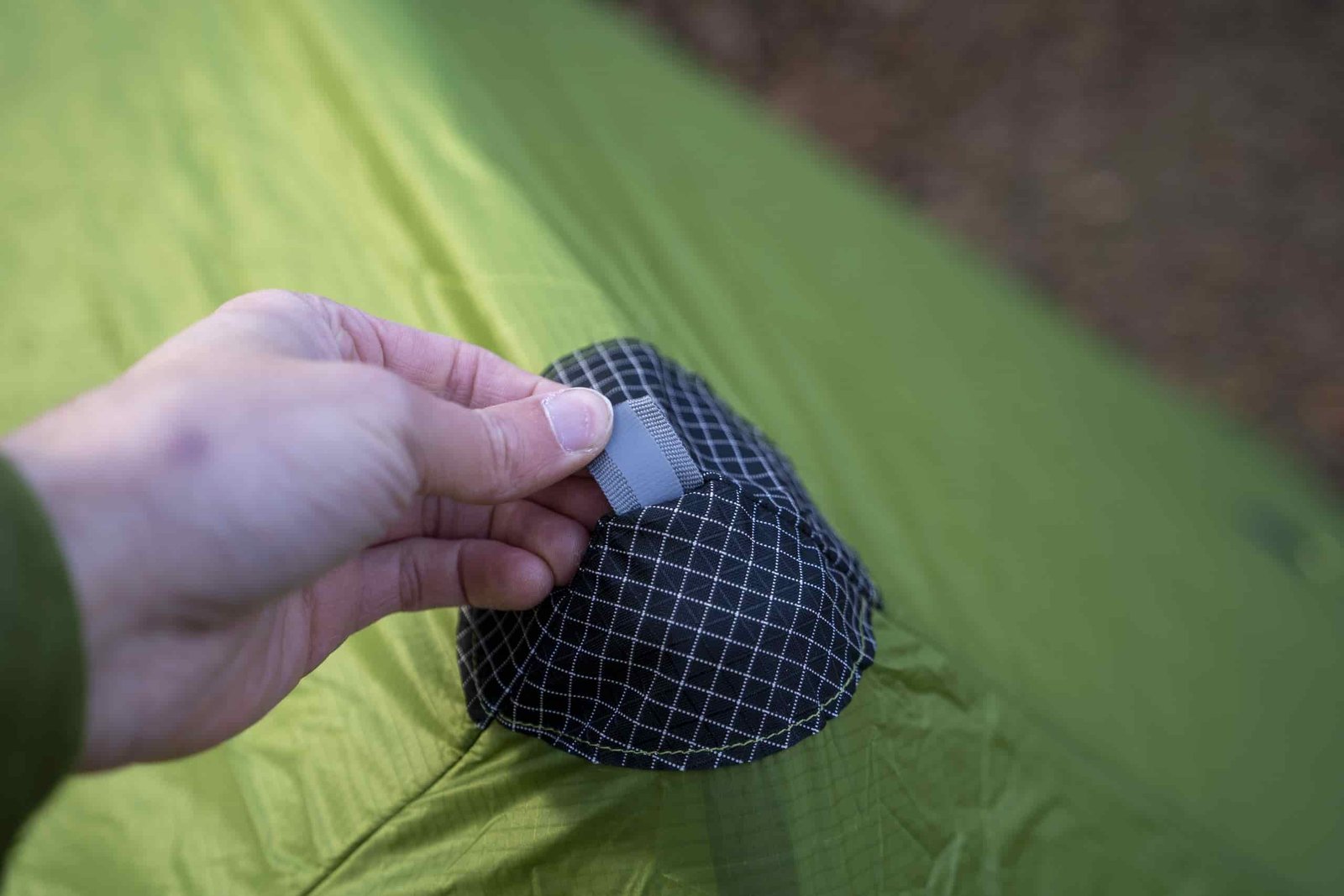 a hand holds a peak guyline attachment point on a green tent
