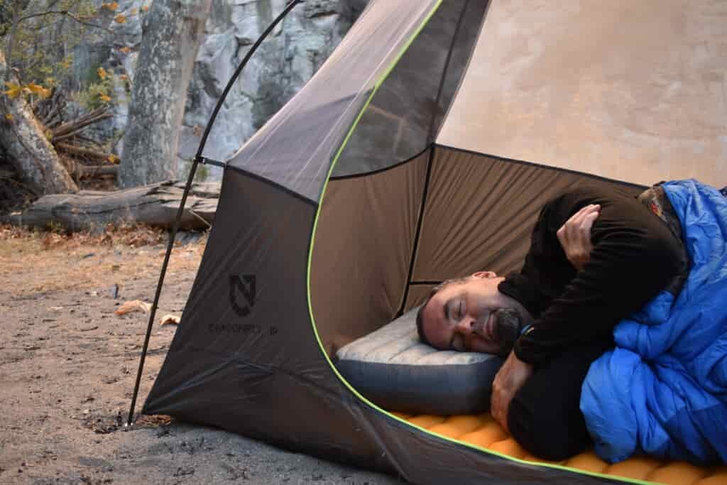 The Aeros Down Deluxe pillow supports the author's head and neck as he sleeps on his side in a tent pitched in front of gray cliffs