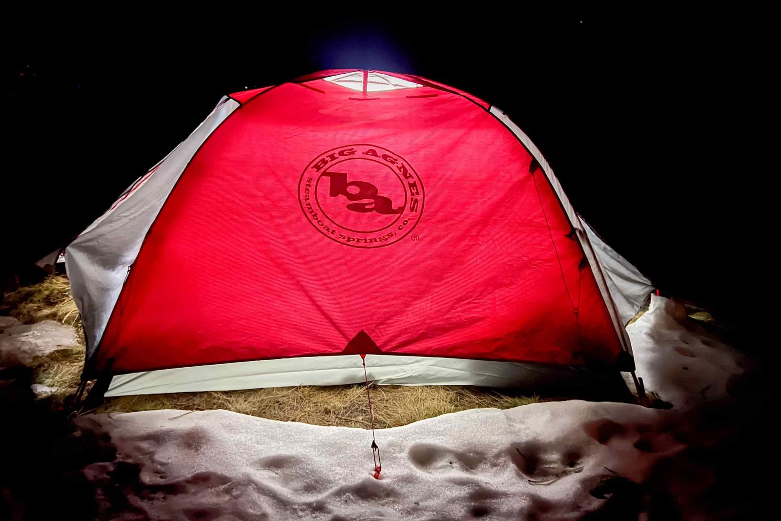 Big Agnes Copper Spur Expedition tent glowing red at night in a snowy setting with a reflective logo visible.