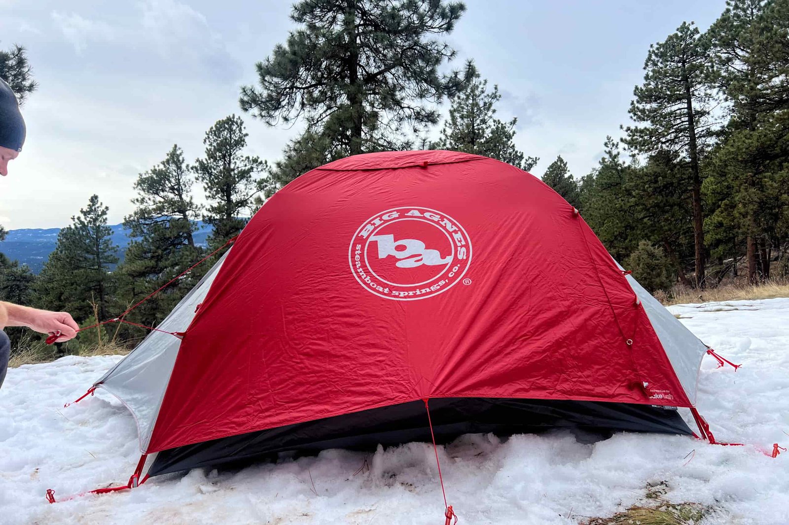 Big Agnes Copper Spur Expedition tent with a red rainfly set up in a snowy forest during daylight.
