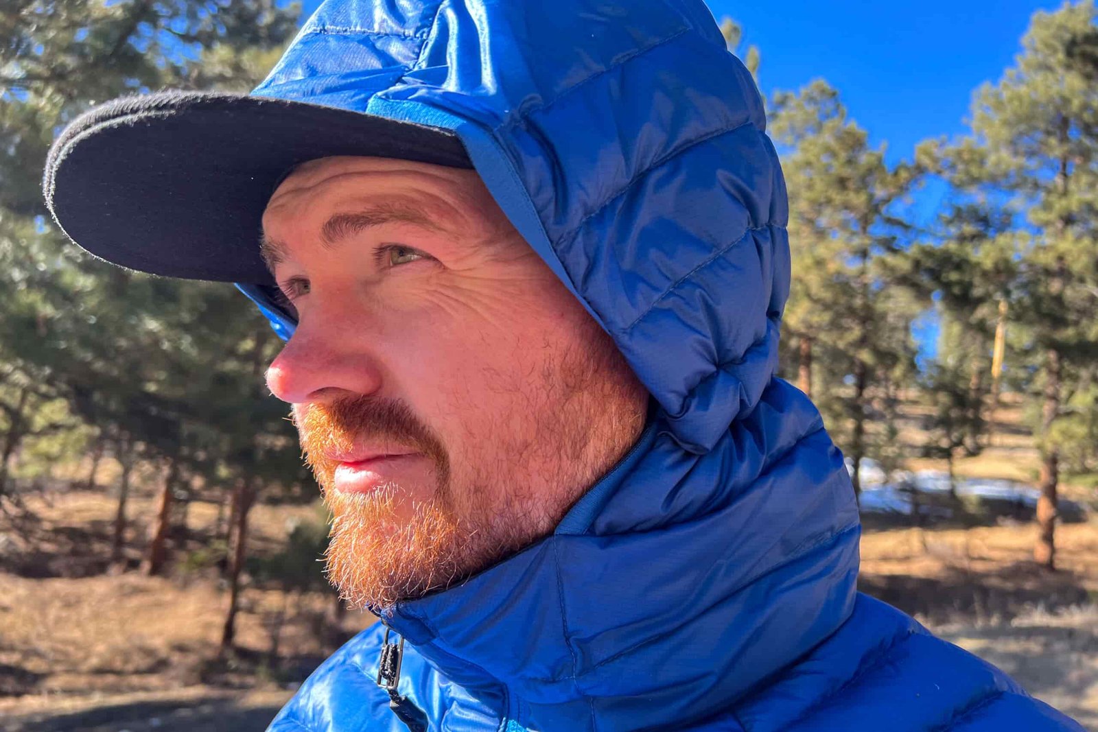 Close-up of a person wearing the Black Diamond Approach Down Hoody with the hood up, showing a snug fit around a baseball cap.