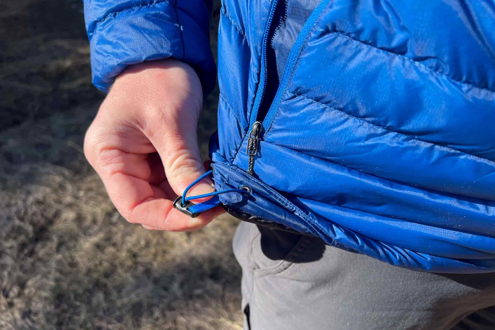 A close-up of a person tightening the hem drawcord of the Black Diamond Approach Down Hoody.