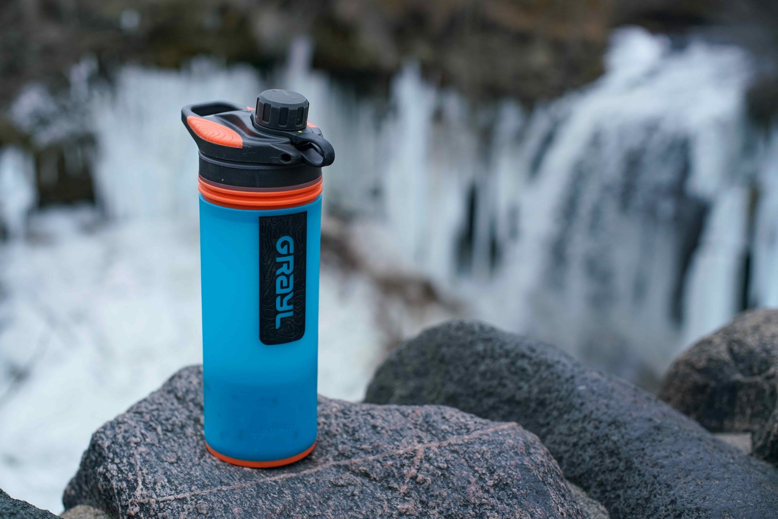The Grayl GeoPress sits on a rock with a partially frozen waterfall in the background.