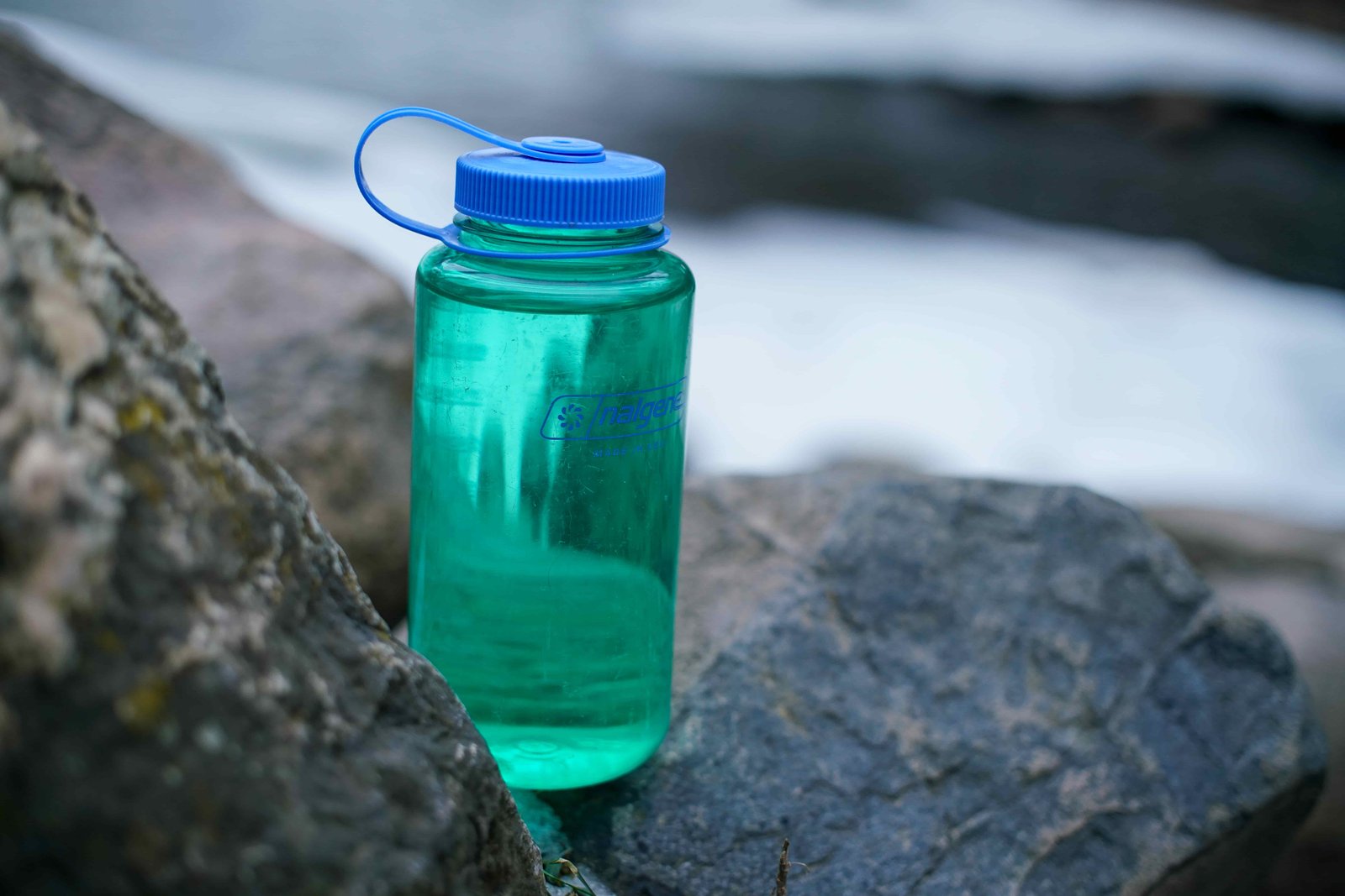The Nalgene Wide Mouth water bottle sits in between two rocks with a partially frozen stream in the background.