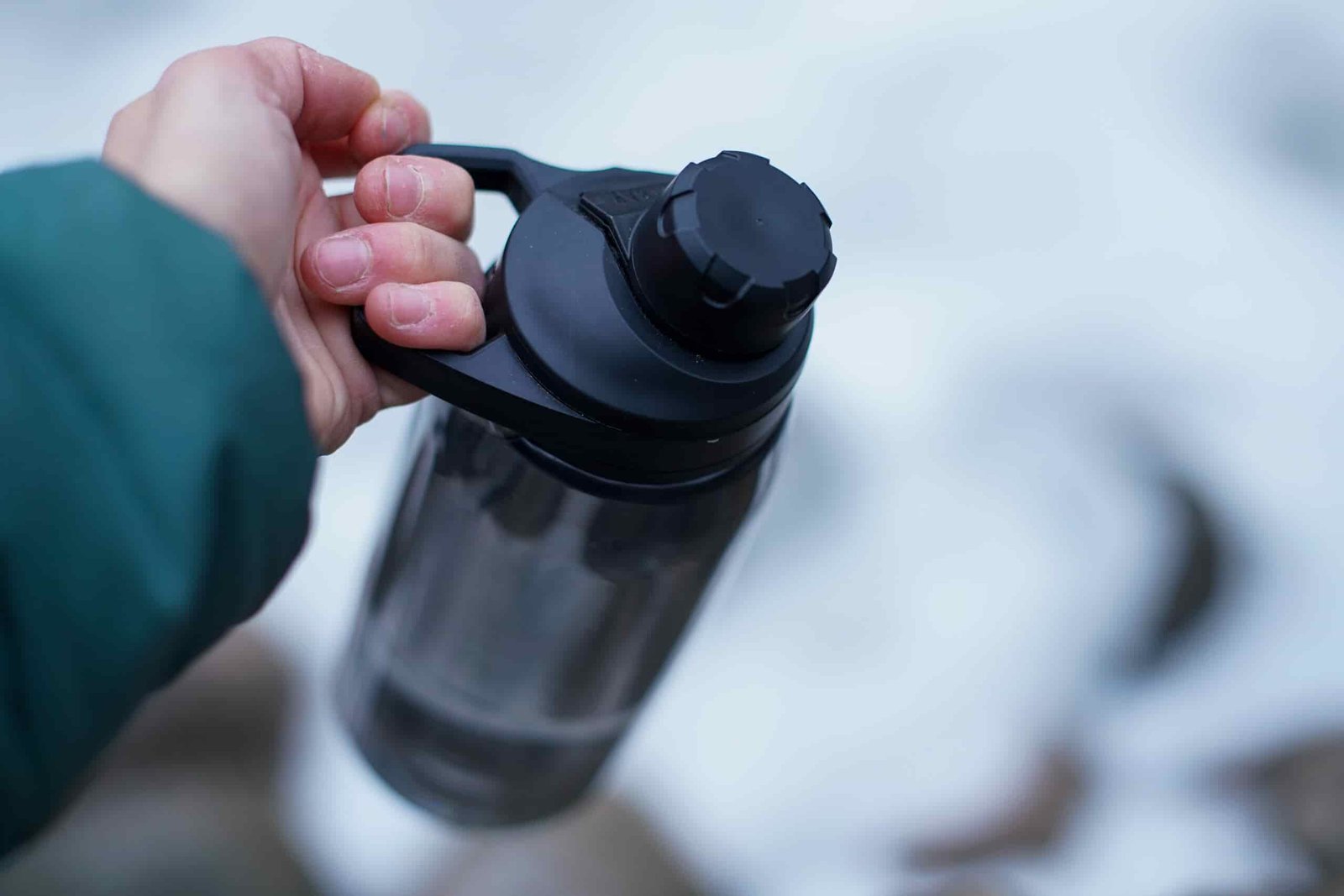 A close up of a hand holding the CamelBak Chute Mag Renew by the handle built into its lid.