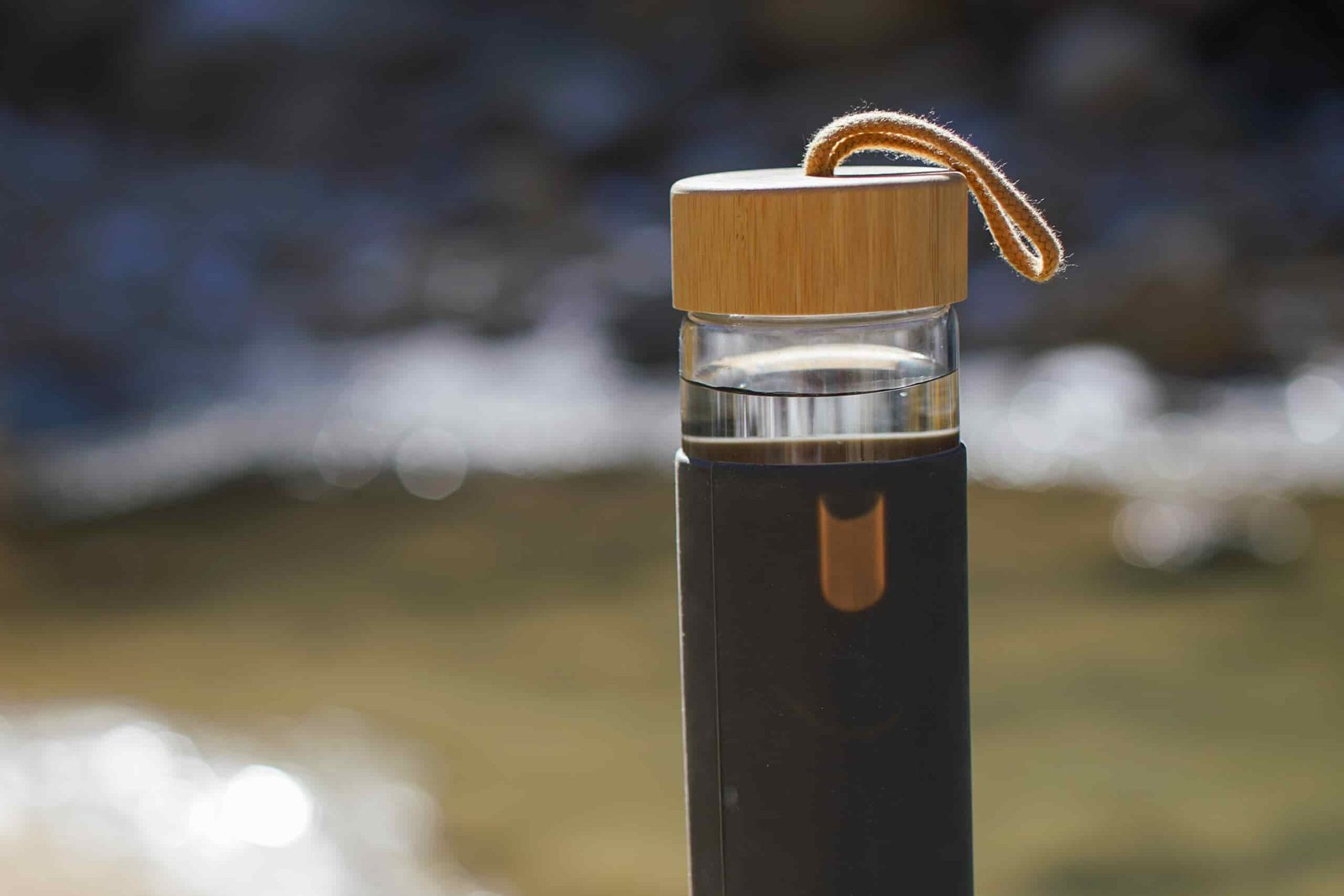 The Yomious Glass water bottle sits on a rock with a river in the background.