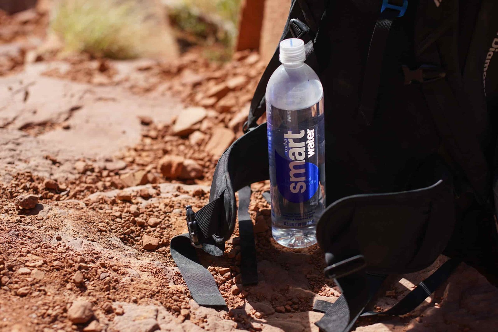 A bottle of Glaceau Smartwater sits on the ground next to a backpack.