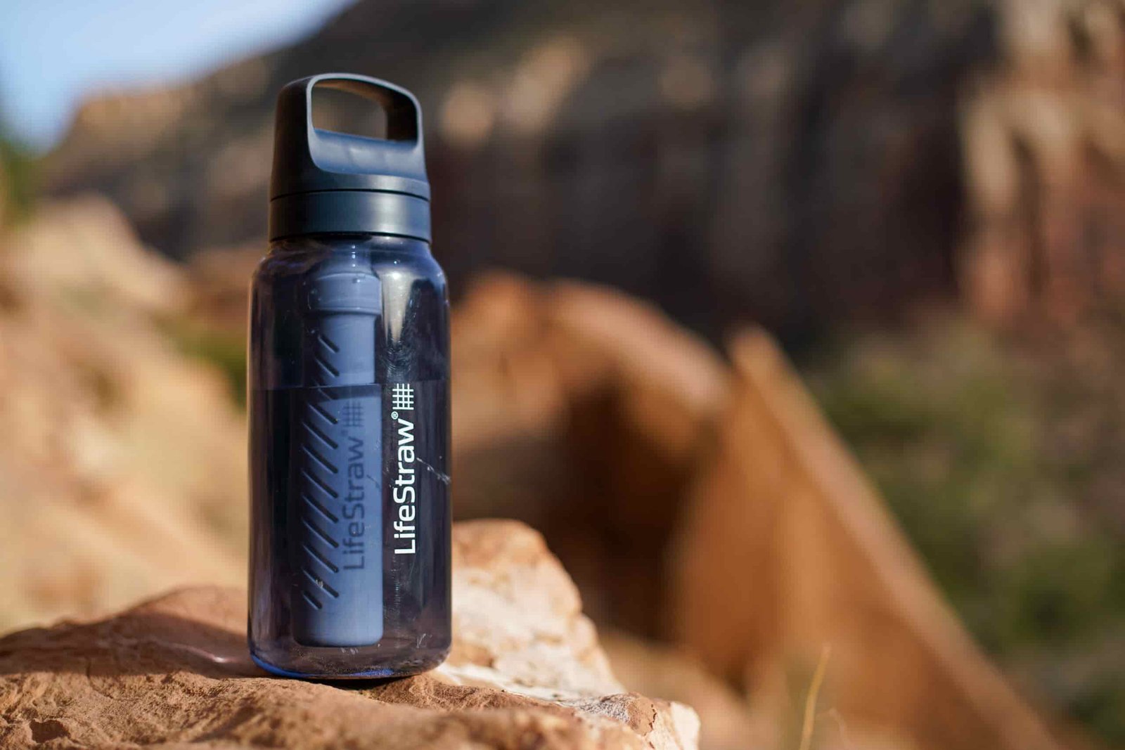 The LifeStraw Go Series water bottle sits on a rock with a mesa in the background.