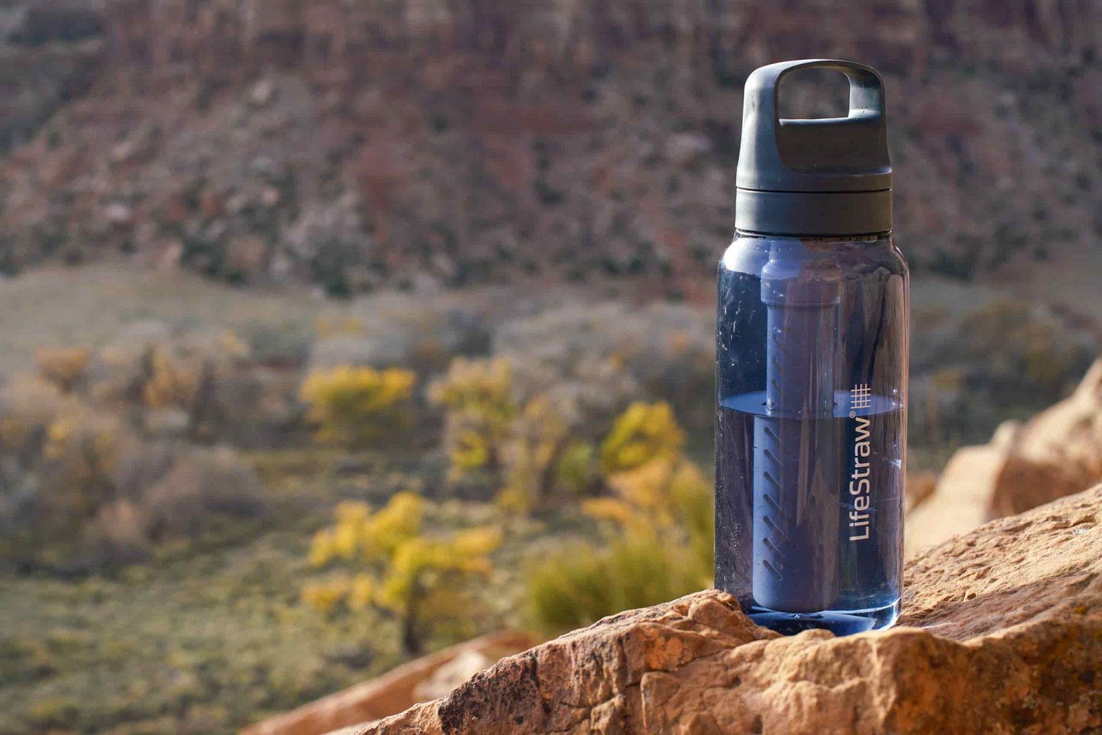 The LifeStraw Go Series water bottle sits on a rock with a mesa in the background.