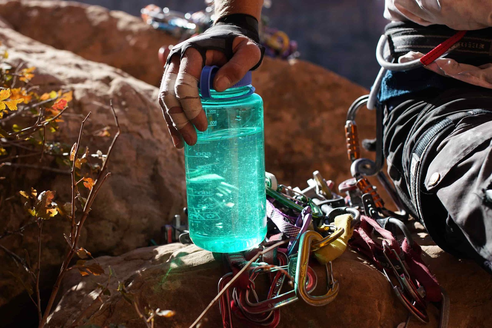 A close up of a person's hand resting on top of the Nalgene Wide Mouth water bottle. The bottle sits on a pile of climbing gear.