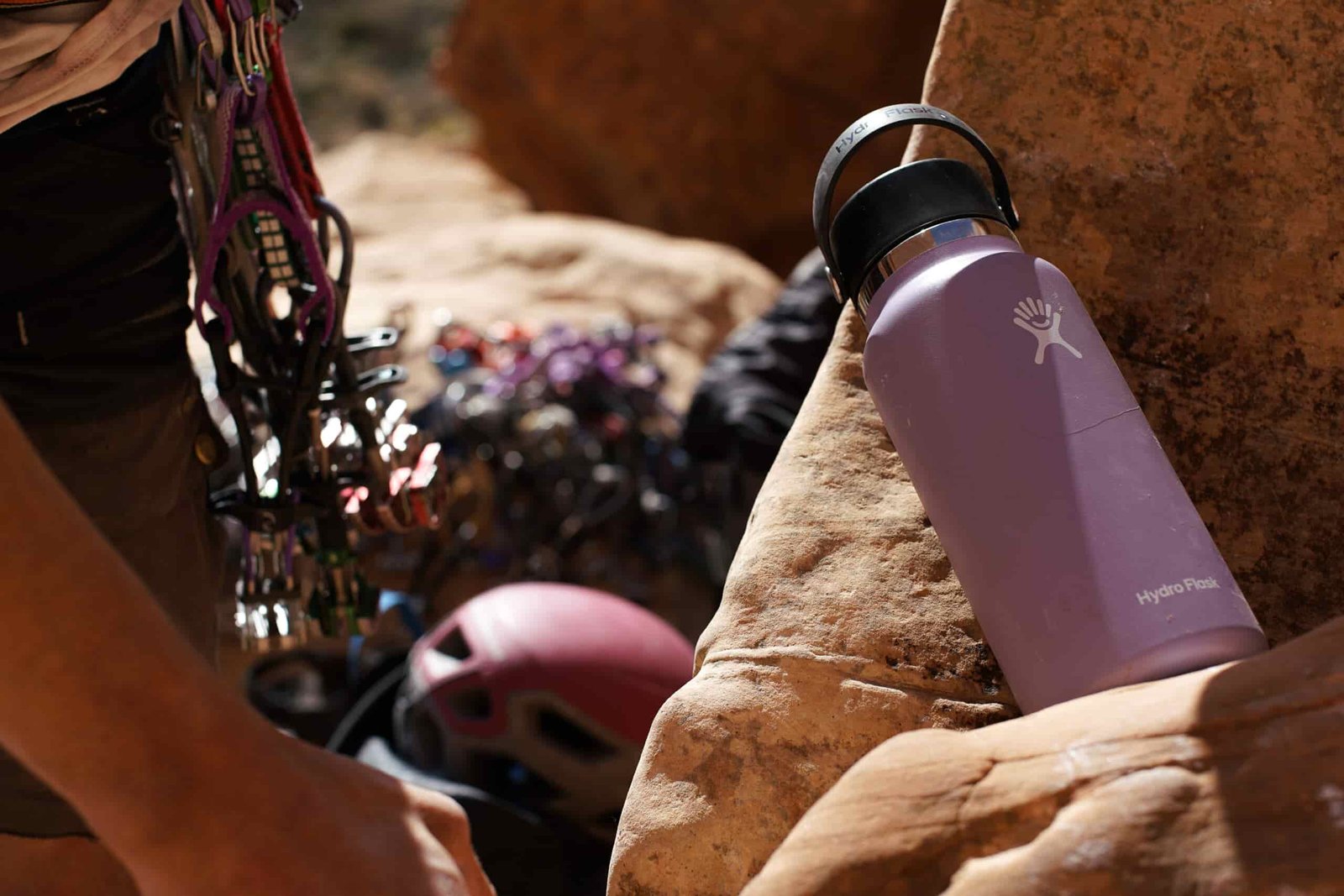 The Hydro Flask Wide Mouth sits on a rock with a person wearing a climbing harness partially visible.