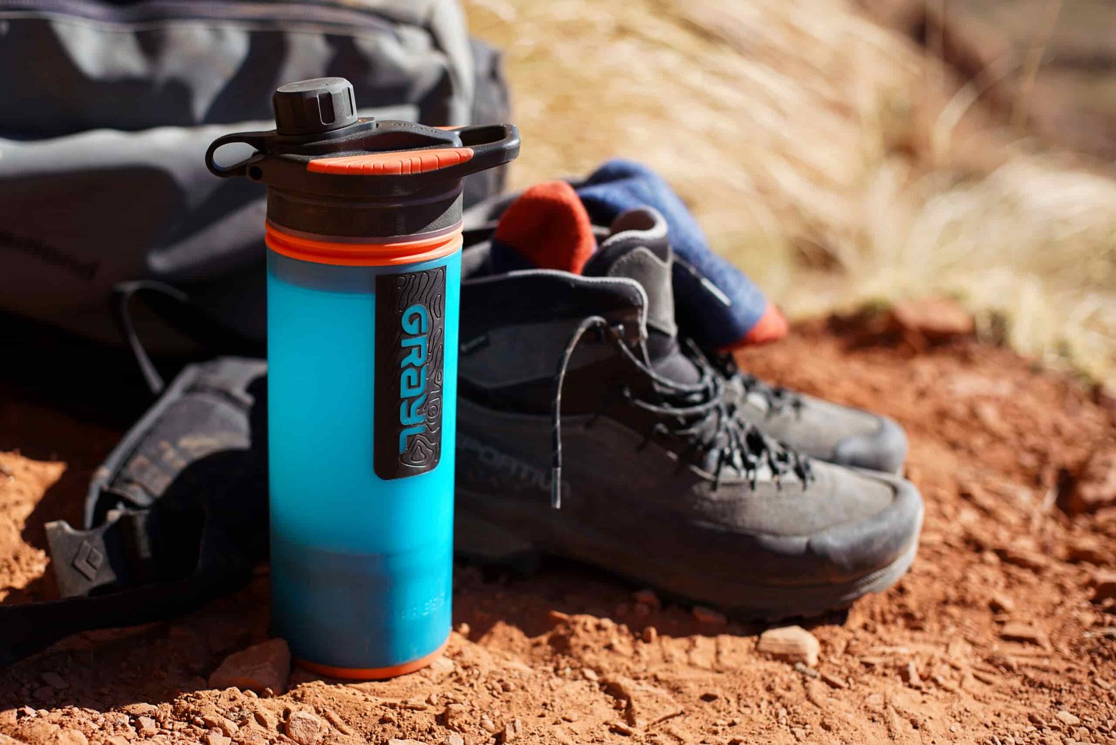 The Grayl GeoPress water bottle sits on the ground next to a pair of hiking boots and a backpack.