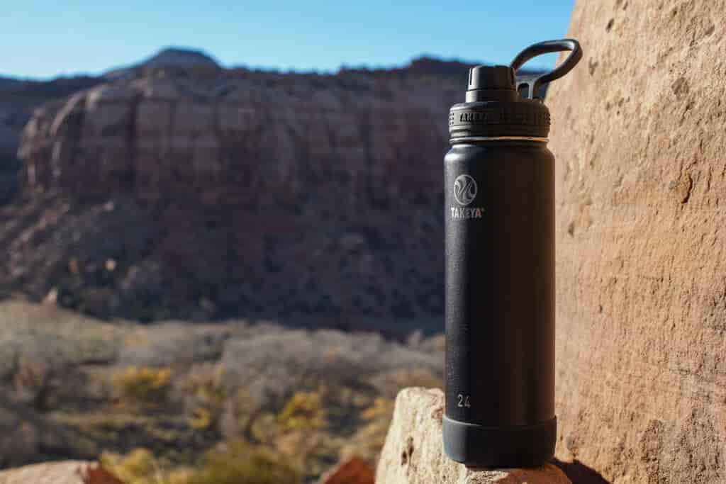 The Takeya Actives Insulated water bottle sits on a rock with a mesa in the background.