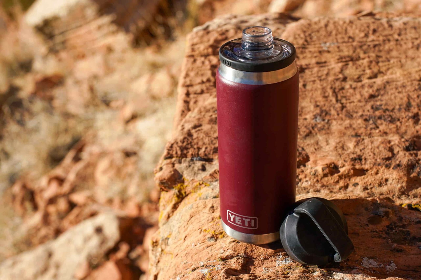 The YETI Rambler sits on a rock with its lid beside it.