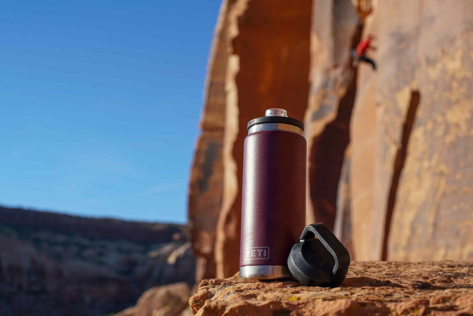 The YETI Rambler sits on a rock with a climber on the rock face behind it.