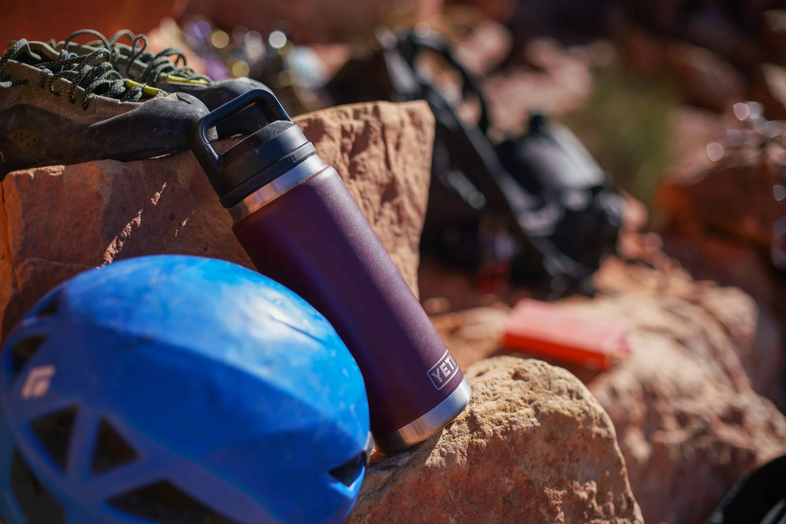 The YETI Rambler sits on a rock with a pair of climbing shoes, helmet, and backpack next to it.
