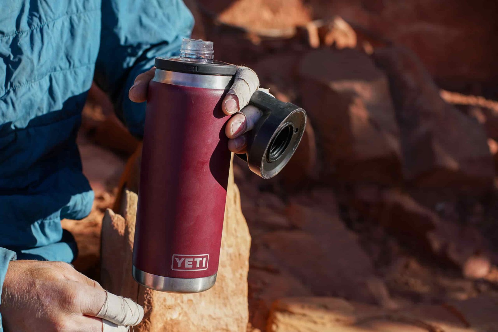 A close up of a person with fingers taped for crack climbing holding an open YETI Rambler water bottle in their hand.