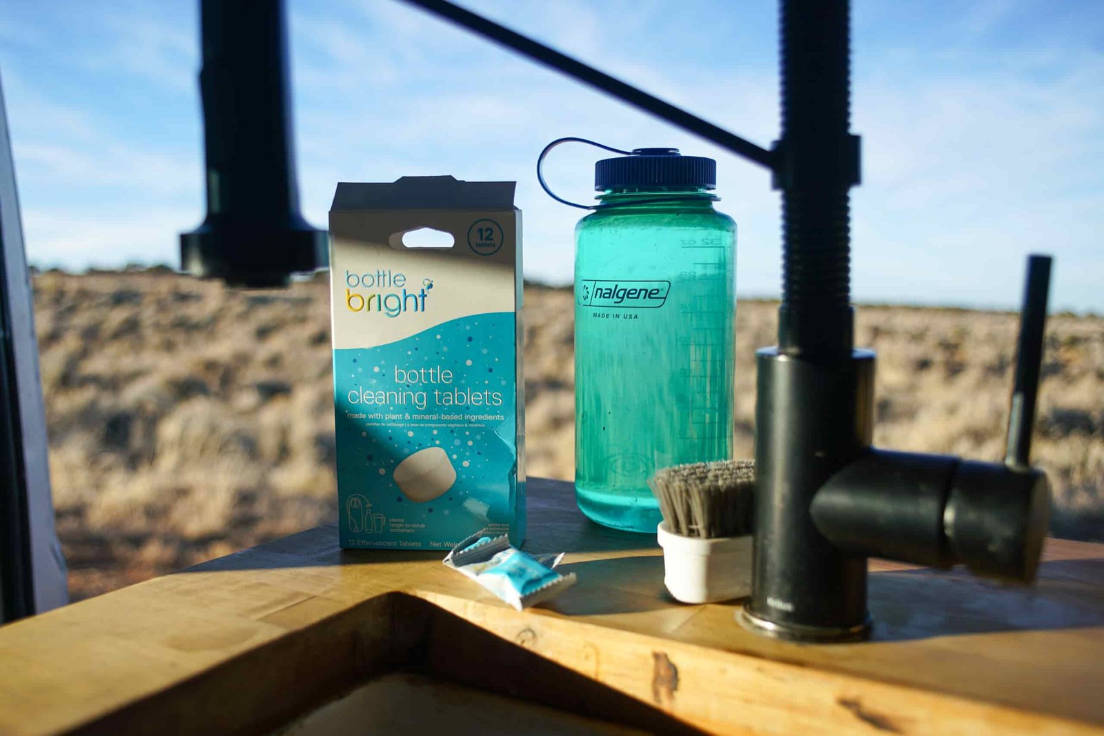 The Nalgene Wide Mouth water bottle and a box of Bottle Bright bottle cleaning tablets sit at the corner of a sink with a desert expanse in the background.